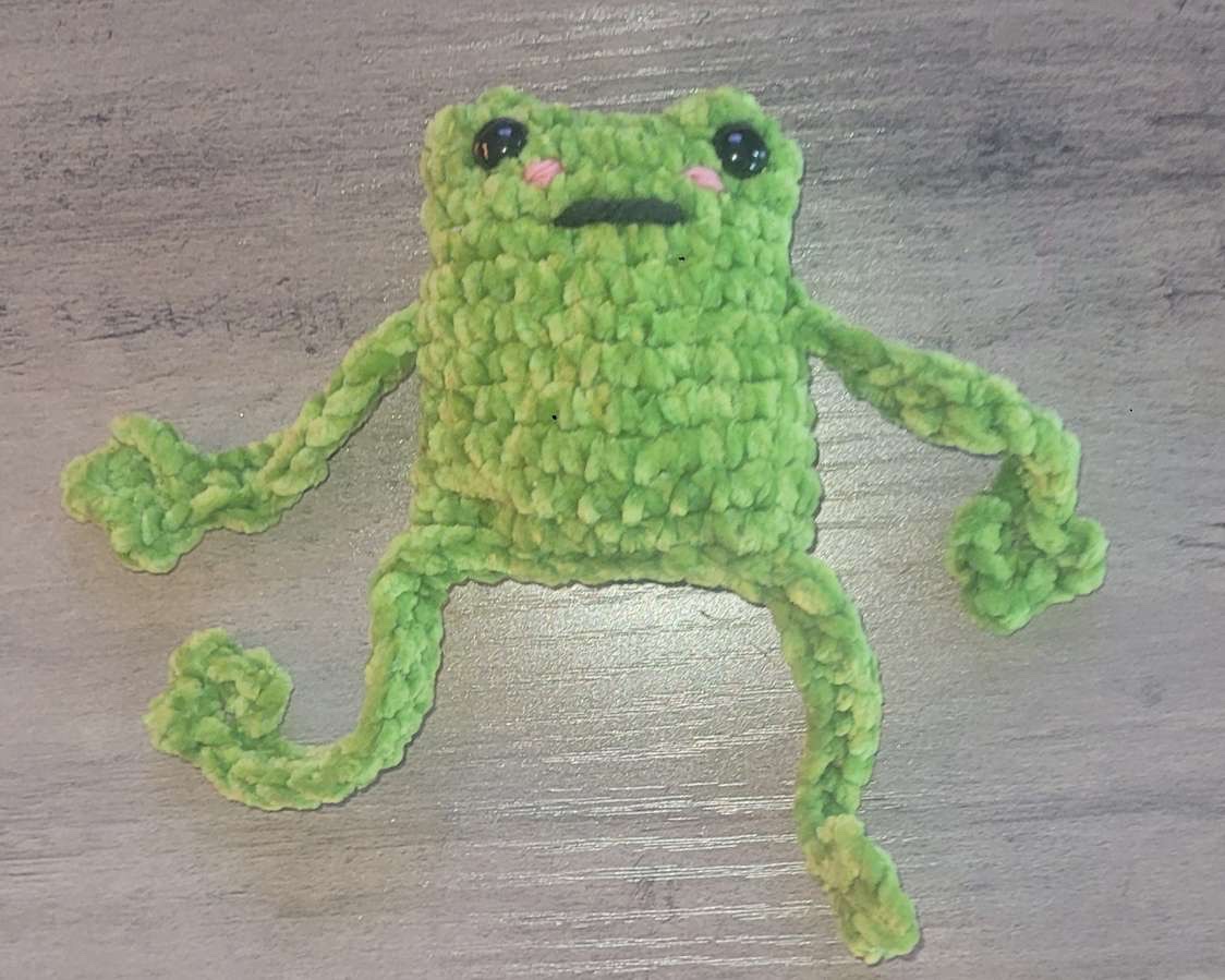 Small green plush crocheted frog with long curly legs and pink cheeks
